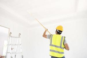 A view of the painter behind the wall painter with a paint roller and split bucket on a large empty space with a wooden staircase. photo