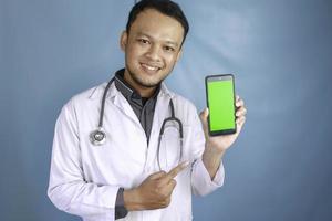 Young Asian man doctor is showing green screen or copy space on his smartphone photo