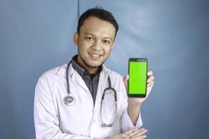 Young Asian man doctor is showing green screen or copy space on his smartphone photo