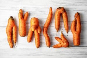 Ugly carrots lie on a light wooden surface photo