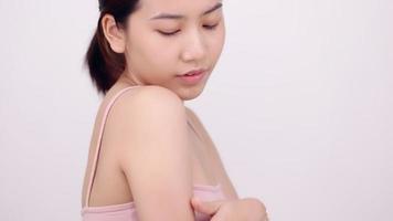 Slow motion of Asian girl with natural make up looking to camera and patting her body gently on white background.