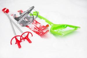 Children's red skis with sticks and a green snow shovel -layout in the snow. Winter outdoor activities, family fun. White natural frosty background. Copy space photo