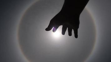 Aerial view of the sun with a circular rainbow surrounded by bright skies and white clouds with shadows of outstretched hands. Phenomenon, sun halo. Natural background in motion. video