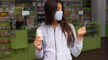 Woman wearing a mask holds and show medication at pharmacy