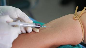 Lab technician holding blood tube sample for study, pricking needle syringe in the arm patient drawing blood sample for blood test. video