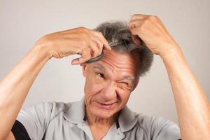 hombre maduro tratando de cortarse el pelo con unas tijeras foto