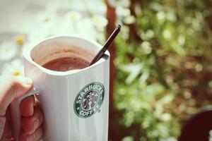 taza de café starbucks colocada sobre rocas alrededor de una fogata de camping con fondo borroso, tonos modernos. foto