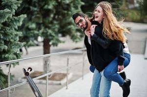 Cool multiracial couple posing with longboard. European girl jumped over shoulder arabian man. photo