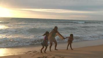 felice famiglia asiatica di madre e figlie divertendosi a giocare sulla spiaggia durante le vacanze estive al tramonto. gita estiva in famiglia al mare. concetto di viaggio e vacanza. video