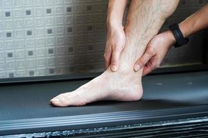 Asian man hurts his ankle while running on a treadmill,concept of not wearing shoes while running on a treadmill photo