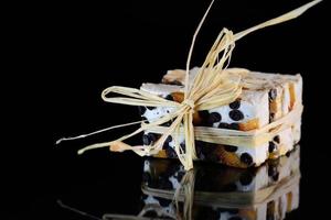 Several pieces of torrone or white nougat with nuts, candied fruits and chocolate are tied together with raffia and lie on a reflective surface in front of a dark background photo