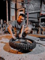 an old man in short shorts is trying hard to change the rear motorcycle tire at night in his workshop.  photo taken at night outdoors in luhu village, gorontalo on august 21, 2022