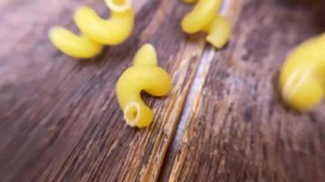 Spiral pasta in brown bowl, scattered pasta on wooden table. Top view video