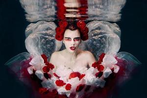 Woman in dress made of white and red roses underwater. Fairy tale, art, fashion concept photo