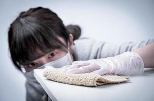 una joven ama de casa está limpiando, limpiando la superficie de la mesa de casa para detener la propagación de la infección con un trapo húmedo, antibacteriano, de cerca, estilo de vida. foto