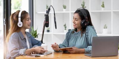 Smile two asian young woman, man radio hosts in headphones, microphone while talk, conversation, recording podcast in broadcasting at studio together. Technology of making record audio concept. photo