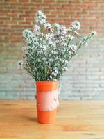 Closeup a Beautiful flowers in vase on wooden table and blurry brick wall background. photo