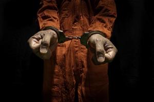 esposas al criminal acusado con mono naranja de la cárcel. delincuente de la ley condenado a cumplir condena en la cárcel, de fondo negro foto