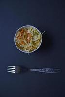 Delicious salad of vegetables and sauces in a salad bowl with a fork. Salad on a black background. photo