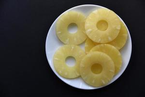 deliciosos anillos de piña fresca en un plato sobre un fondo negro. delicioso desayuno de anillos de piña. foto