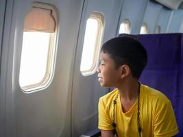 un niño asiático se sienta y sonríe y mira por la ventana de un avión. foto