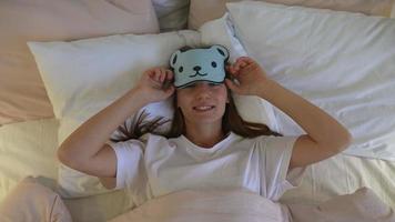 joven hermosa mujer en la cama se pone una máscara para dormir con forma de oso video