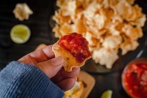 Close up Hand hold chip dip tomato salsa with plate with taco, nachos chips and tomato dip. Spicy Nachos  on rustic wooden background photo