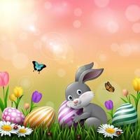 Easter greeting card with a little rabbit, colorful eggs and flowers in the grass