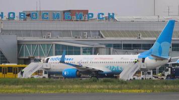 NOVOSIBIRSK, RUSSIAN FEDERATION JULY 15, 2022 - Passenger plane Boeing 737 Pobeda Airlines at the terminal of Tolmachevo airport. Airport employees climb the stairs to the plane video