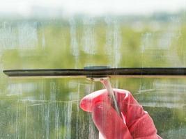 hand in pink glove washes window glass by squeegee photo