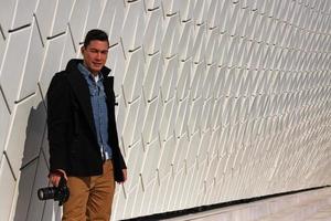 Man standing in front of a white wall with a camera in his hand photo