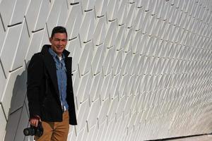 Man standing in front of a white wall with a camera in his hand photo