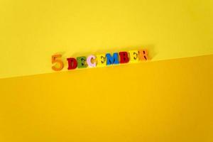 5 de diciembre sobre fondo amarillo y papel con letras de madera y multicolores con espacio para texto. foto