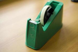 Used green tape dispenser with transparent tape on a wood background. photo