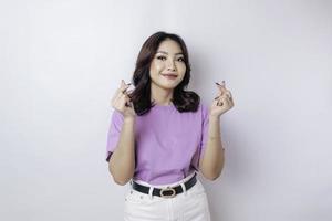 una atractiva joven asiática con una camiseta morada lila se siente feliz y un gesto romántico del corazón expresa sentimientos tiernos foto