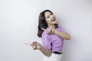 hermosa mujer asiática sonriente señalando con el dedo el espacio vacío al lado de su aislado fondo blanco foto