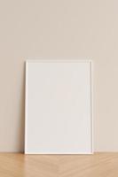Clean and minimalist front view vertical white photo or poster frame mockup leaning against wall on wooden floor. 3d rendering.