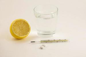 Glass of water, pills, lemon and thermometer on white background. Glass mercury thermometer with a high temperature. Concept illness, colds, cure, fall and winter. photo