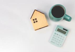 diseño plano del modelo de casa de madera, taza azul de café negro, calculadora azul sobre fondo blanco con espacio de copia. concepto de compra de vivienda. foto