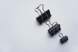 Three black binder clips of various sizes used to staple documents against photo