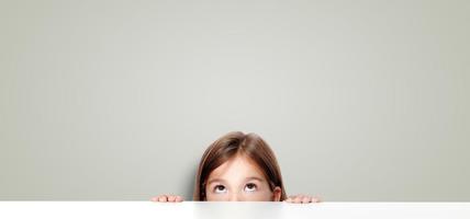 linda niña pequeña mirando hacia arriba en el escritorio de la escuela. foto