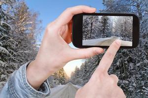 tourist taking photo of winter road in snow forest