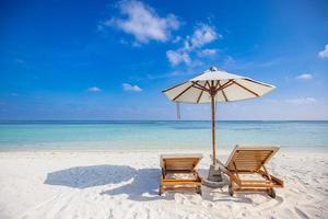 Beautiful tropical island scenery, two sun beds, loungers, umbrella under palm tree. White sand, sea shore horizon, idyllic blue sky, calm relax. Amazing beach resort hotel. Couple reactional retreat