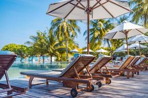 Umbrellas and chairs around outdoor swimming pool in resort hotel for vacation leisure lifestyle. Luxury destination concept, lounge closeup scenic under palm trees, relax, tranquil vibes photo