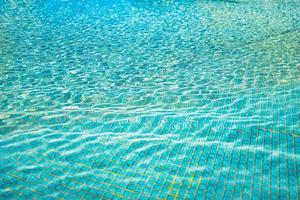 Relaxing surface of blue swimming pool, background of water. Ripples, small waves of water in swimming pool with sunny bright light. Shining blue water ripple background photo