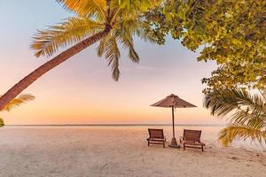 Sunset beach. Beautiful tropical island shore, two sun beds lounger, parasol under palm tree. Sand sea horizon, colorful dream sky, calm relax. Summer vacation beach landscape. Romantic couple resort photo