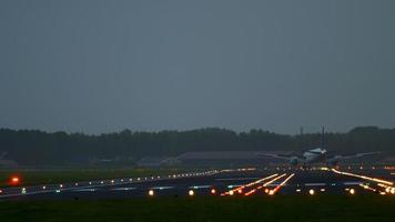The wide bodied aircraft lands on the illuminated runway in the early morning video