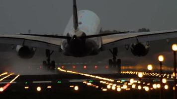 The wide bodied aircraft lands on the illuminated runway in the early morning video