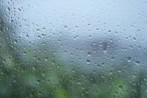 Unfocus background rain drops on window with green tree and blue sky. photo