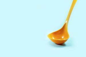 yellow ladle used to scoop soup isolated on a turquoise photo